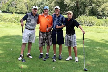 Four golfers on a golf course posing for a photo holding golf clubs